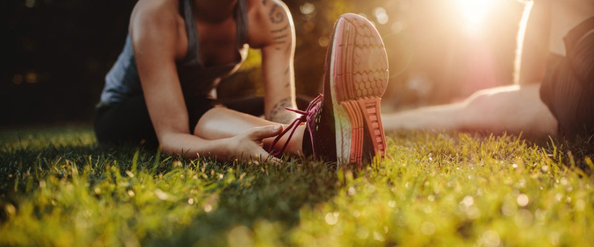 Cropped shot of fit young woman stretching at park with man. Focus on feet of female.